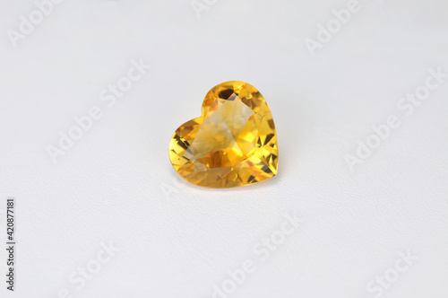 Natural yellow citrine heart shaped loose faceted gemstone on white background. Shiny polished stone quartz group mineral gradient zoned color pattern. Photo for articles on the topic of gemology.