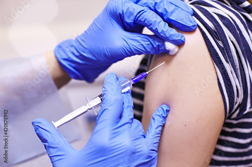 Doctor or nurse giving shot or vaccine to a patient s shoulder. Vaccination and prevention against flu or virus pandemic. Doctor in gloves holding syringe and making injection to patient. 