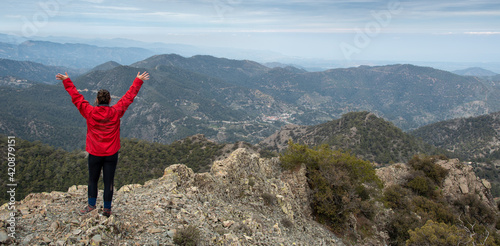 Back view of a backpacker woman with raised arms standing on rocky top enjoying mountain range panorama. photo