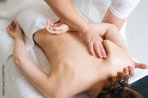Top view of male masseur massaging back and shoulder blades of young woman lying on massage table on white background. Concept of massage spa treatments.