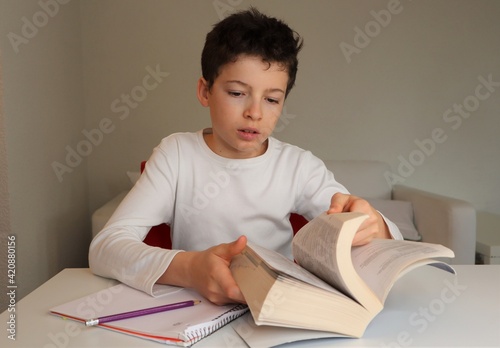 Foto Boy with light skin and brown hair doing homework, flipping pages and looking up a word in a dictionary