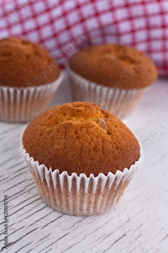 Morning breakfast vanilla muffins in white paper cups on a white wooden cutting board, white background, close-up view 