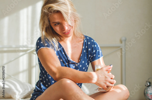 Beautiful woman drinking a coffee sitting on bed. Blonde, tranquil, relaxed and peaceful woman at home. Cozy morning and daily routine - coffee in bed. Vacation, enjoyment and well being