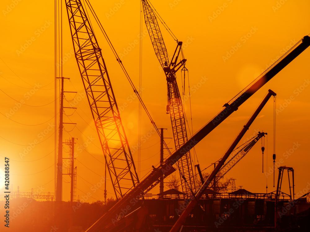 Arrows of construction cranes on orange sunset background. Construction machinery at the construction site. Background for advertising or website