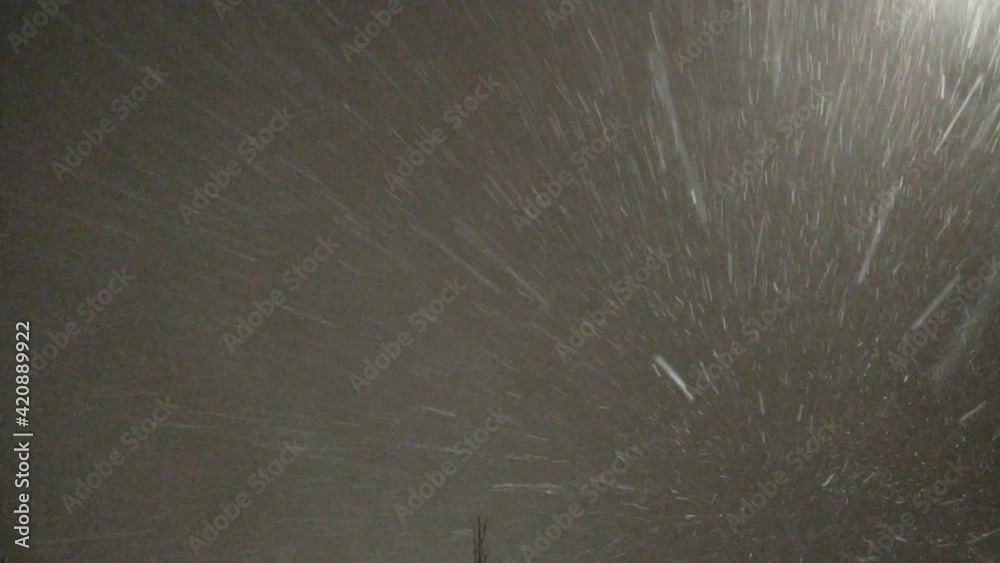 Evening dark sky light of street lamps and snowstorm. It is snowing and a strong wind is blowing, snowflakes fly by like thin white lines in the light of a street lamp. The winds chaotically carry sno