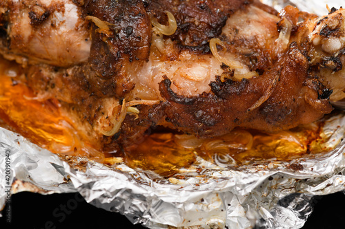baked meat and fried onions on a baking sheet, pork ham on foil and wooden background, home cooking