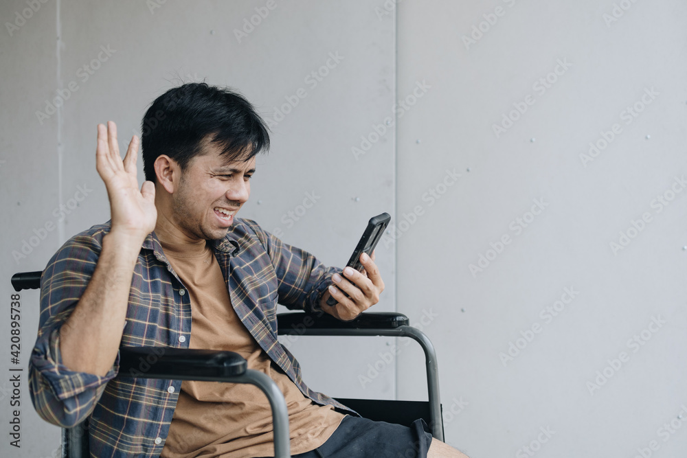 Asian man holding smartphone and conference call sitting on wheelchair Asian man holding smartphone and conference call sitting on wheelchair