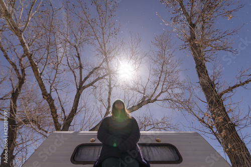 Woman beside campervan, bare trees in background