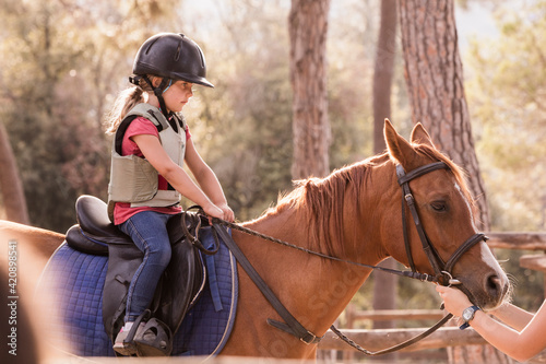 Girl learning to ride horse in paddock