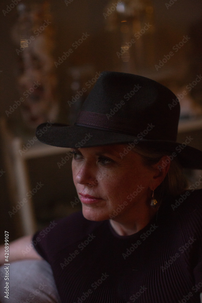 Stylish mature woman wearing trilby sitting on sofa, low key portrait Stylish mature woman wearing trilby sitting on sofa, low key portrait