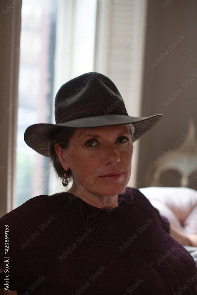 Stylish mature woman wearing trilby sitting on sofa, portrait Stylish mature woman wearing trilby sitting on sofa, portrait