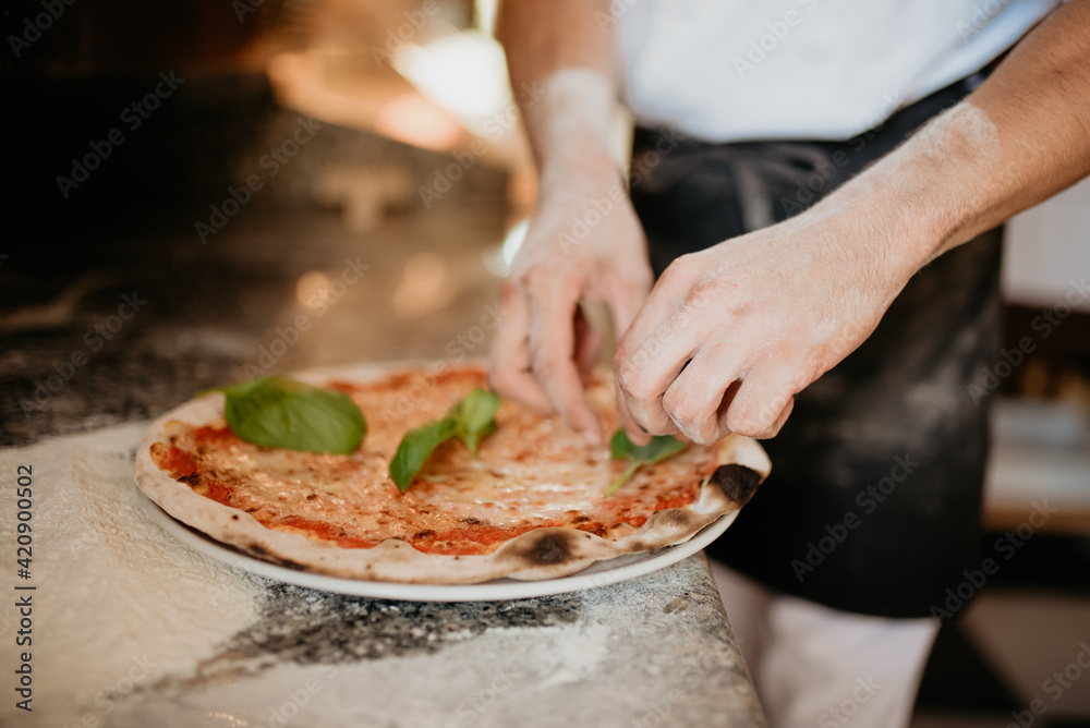 Chef garnishing pizza with basil leaves on kitchen worktop