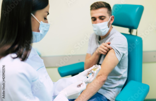The doctor in the medical mask is preparing for man vaccination shot  medicine  and drug concept.