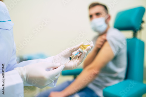 The doctor in the medical mask is preparing for man vaccination shot, medicine, and drug concept.