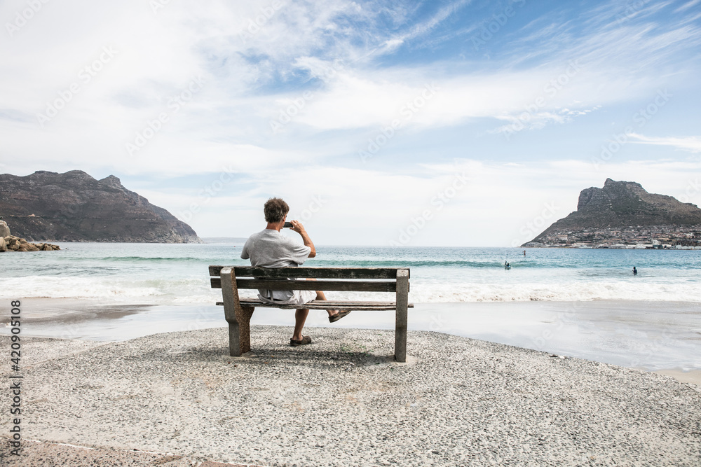 Mature man taking photograph from beach bench, Cape Town, Western Cape, South Africa Mature man taking photograph from beach bench, Cape Town, Western Cape, South Africa