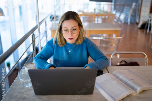 Female higher education student typing on laptop in university cafe
