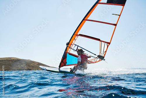 Young man leaning back windsurfing ocean waves, surface level rear view, Limnos, Khios, Greece