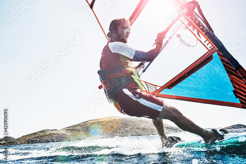 Young man leaning back windsurfing sunlit ocean waves, Limnos, Khios, Greece