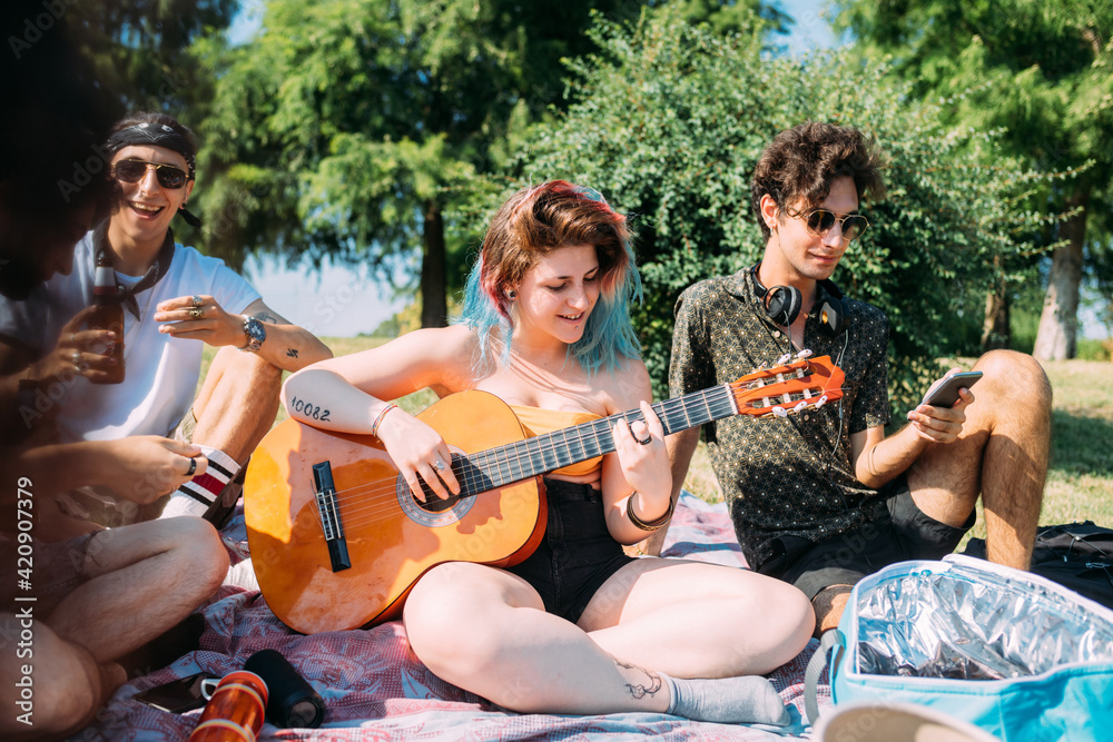 Group of friends relaxing, playing guitar at picnic in park