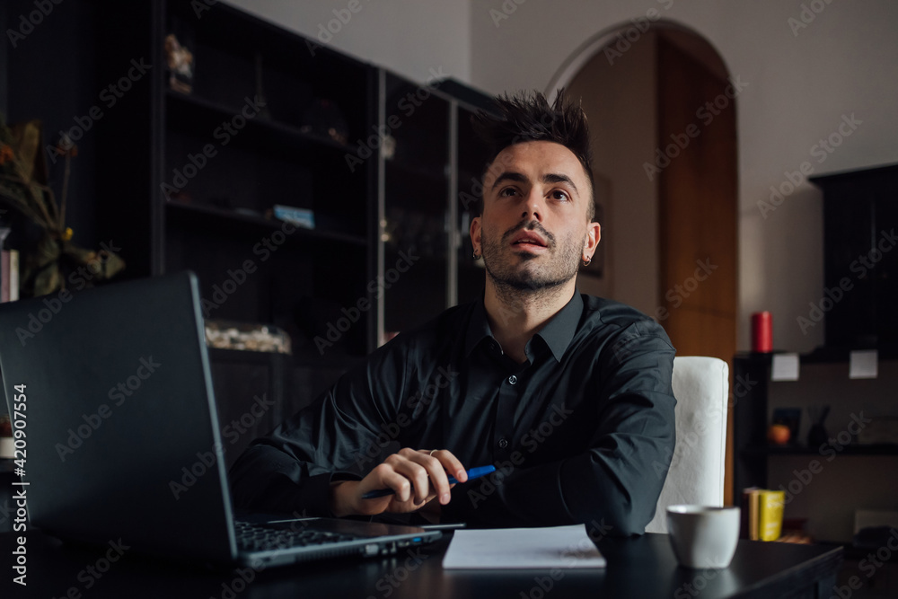 Man looking up while using laptop in home office Man looking up while using laptop in home office