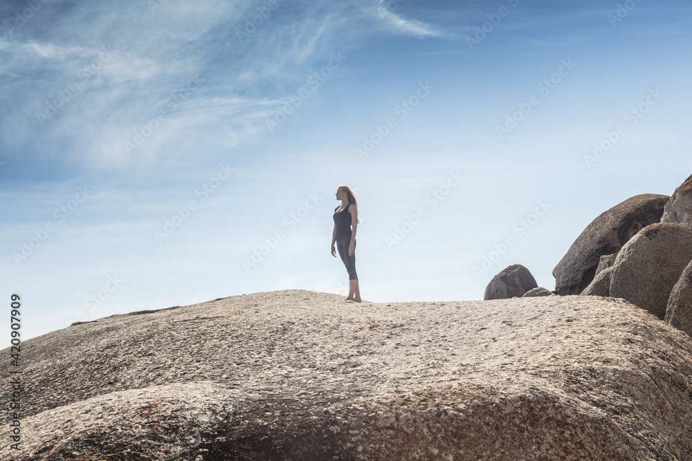 Young woman practicing yoga taking a break looking out from beach boulder, Cape Town, Western Cape, South Africa Young woman practicing yoga taking a break looking out from beach boulder, Cape Town, Western Cape, South Africa