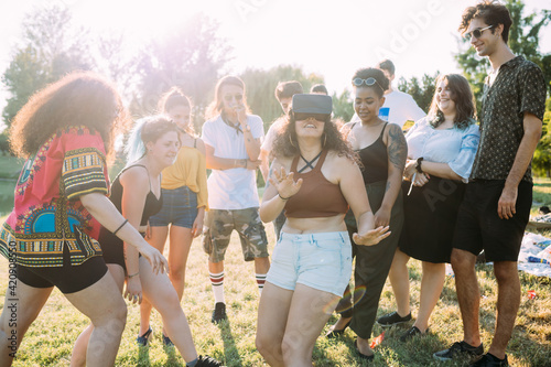 Group of friends teasing woman looking into VR headset in park