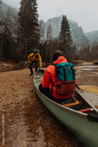 Young canoeing couple pushing off from riverbank, Yosemite Village, California, USA
