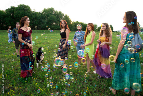 Large group of happy young adults standing in field with floating bubbles photo