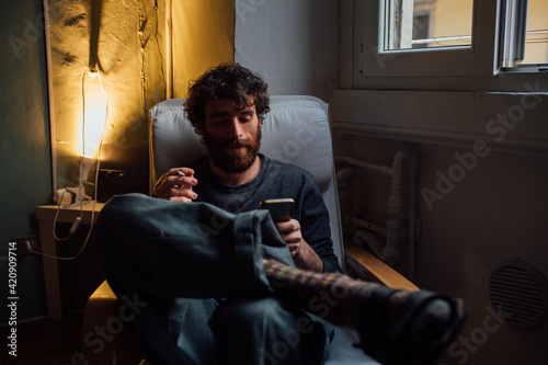 Bearded young man smoking, using smartphone at home