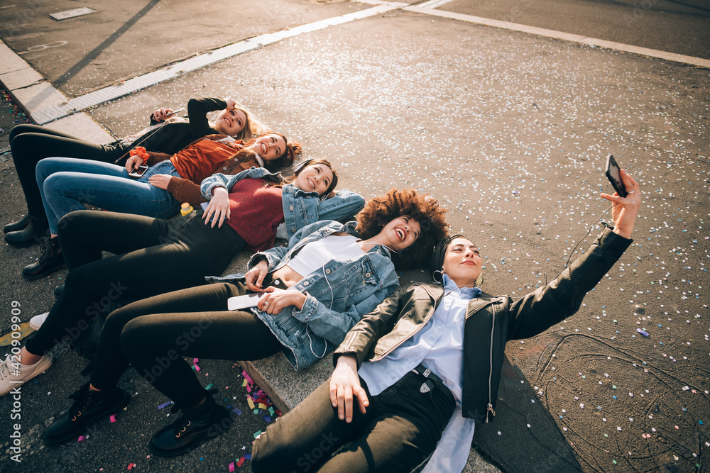Friends together on kerb taking selfie and using smartphones, Milan, Italy