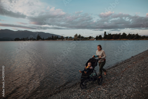Mother with baby in pram walking on beach, Te Anau, Southland, New Zealand