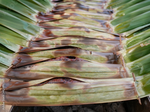 Thai sweetmeat made from flour, coconut and sugar and wrapped with palm leaves on charcoal stove. photo