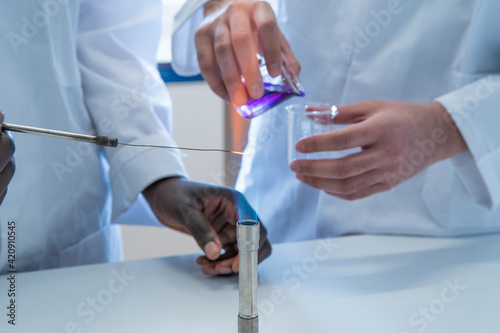 Young female and male scientists experimenting with liquid and bunsen burner in laboratory, cropped photo