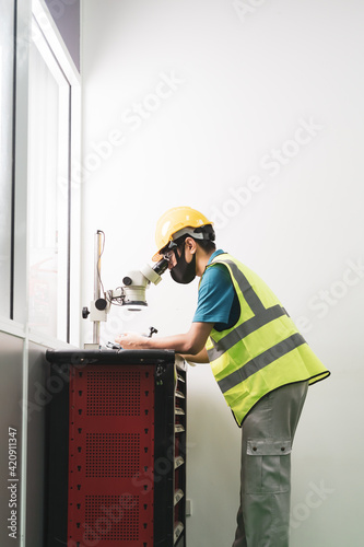 Asian male worker in uniform with vest and hardhat use microscope in factory production line with copy space