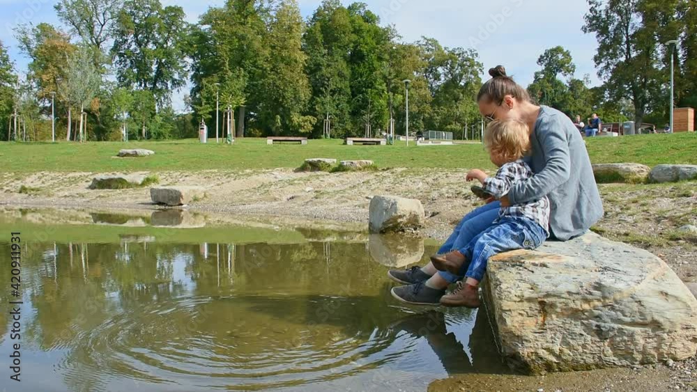 Young mother and cute little child boy having fun throwing stones into the water. Recreational and funny outdoor activity for children in summer Young mother and cute little child boy having fun throwing stones into the water. Recreational and funny outdoor activity for children in summer