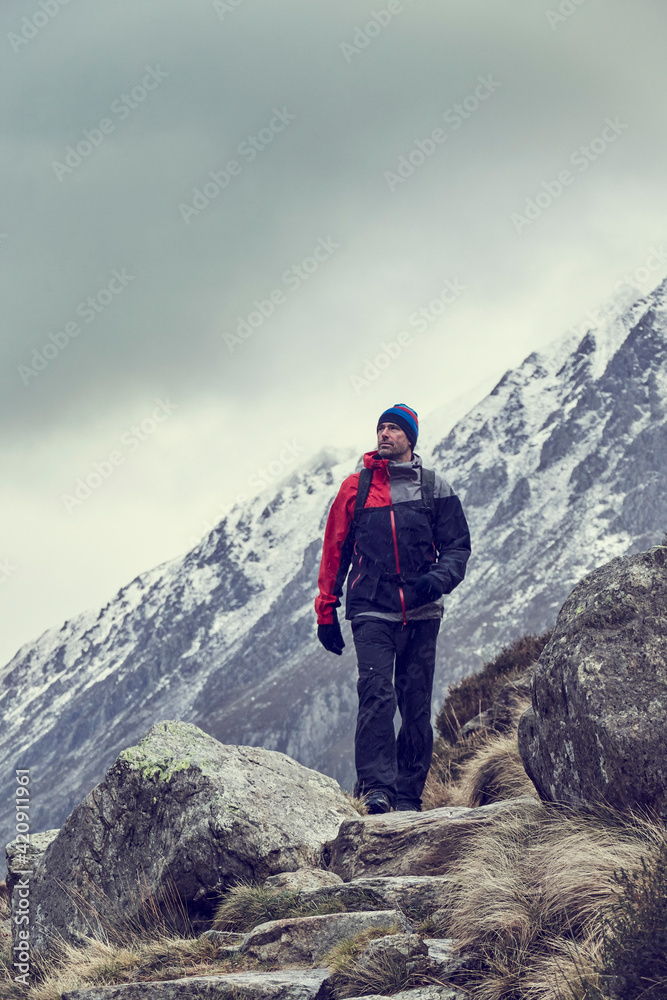Male hiker hiking in rugged landscape with snow capped mountains, Llanberis, Gwynedd, Wales Male hiker hiking in rugged landscape with snow capped mountains, Llanberis, Gwynedd, Wales