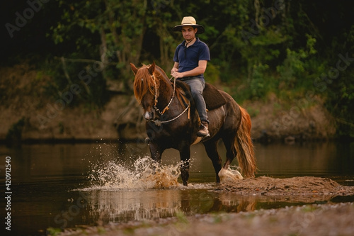 Quadro em tela White man riding a horse inside a river, wearing a straw hat, with his horse in a saddle and throwing water into the air