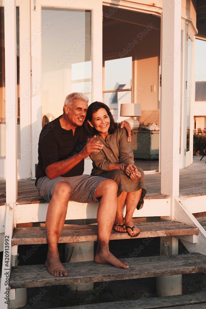 Senior couple enjoying sunset on steps in front of beach house Senior couple enjoying sunset on steps in front of beach house