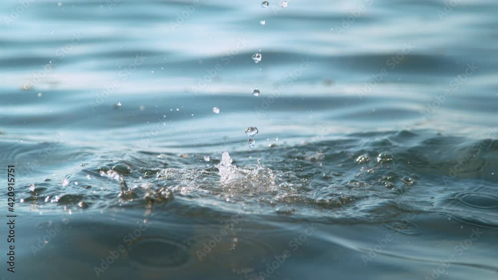 SLOW MOTION, CLOSE UP, DOF: Tiny droplets of crystal clear liquid fall into the endless tranquil ocean. Glassy water is pouring into the calm blue sea. A glass of spring water is poured into vast sea. SLOW MOTION, CLOSE UP, DOF: Tiny droplets of crystal clear liquid fall into the endless tranquil ocean. Glassy water is pouring into the calm blue sea. A glass of spring water is poured into vast sea.