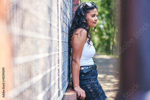 Young woman with long black hair leaning against wall photo