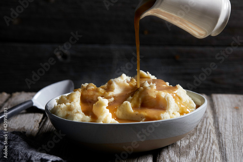 Jug of gravy being poured onto bowl of steaming mashed potatoes, studio shot photo