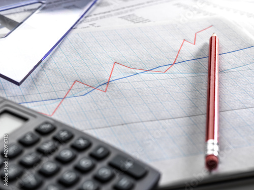 A graph illustrating business data, a red line rising and dipping, and a calculator.  photo