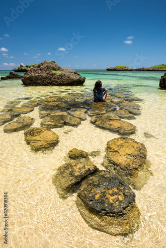 Okinawa girl sitting on the rocks at Hoshizuna beach with its crystal clear waters, Iriomote island.