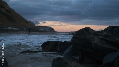 Person Walking Along Beach As Tide Comes In At Sunset photo