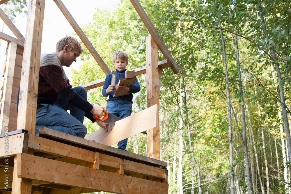 Father and son building treehouse together in garden Father and son building treehouse together in garden