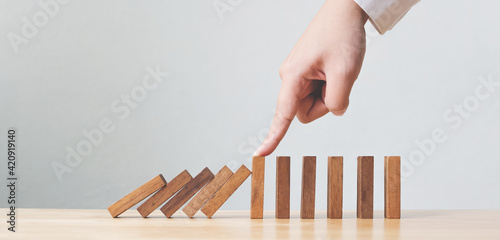 Hand stopping wooden domino business crisis effect or risk protection concept photo