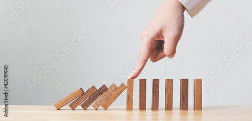 Hand stopping wooden domino business crisis effect or risk protection concept