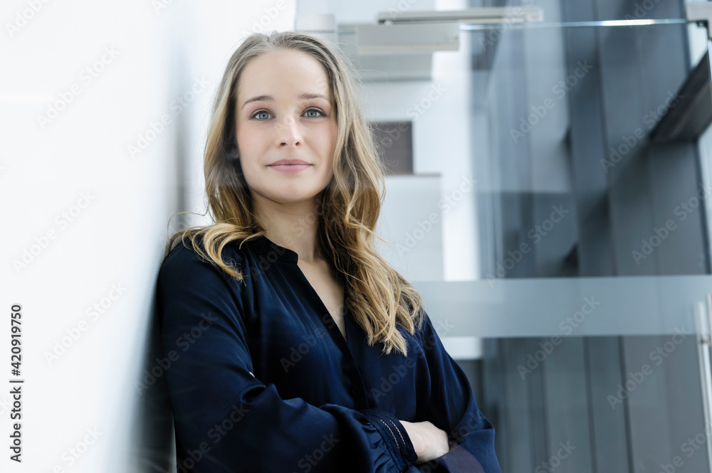Young businesswoman leaning against white wall in office building