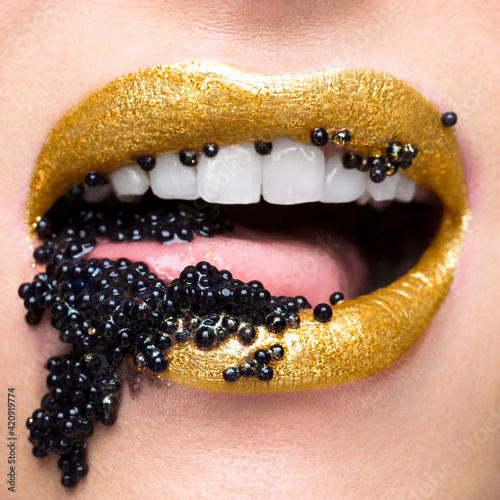 Golden lips with mouthful of black caviar photo