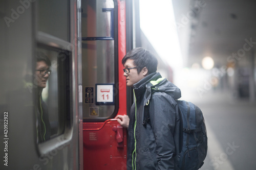 Young Asian man wearing glasses on railway platform, entering passenger train. photo